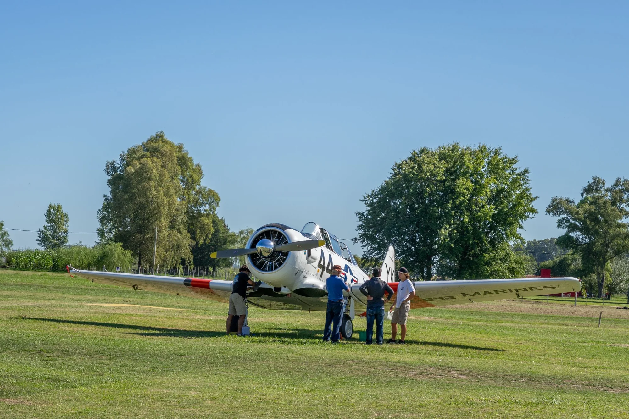 Pilots gathered around a vintage aircraft on a grass field
